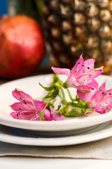 Tropical paradise heaven asian thai pink iris flower on white plate, pineapple, pomegranate on wooden tray in spa resort, restaurant. Holidays rest at sea. Food of gods. Table setting decoration