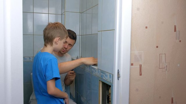 Dad and son make repairs together at home, remove tiles from walls in toilet. Father man explaining boy how to use tools. Self made home repair. Family engaged in construction and renovation work.