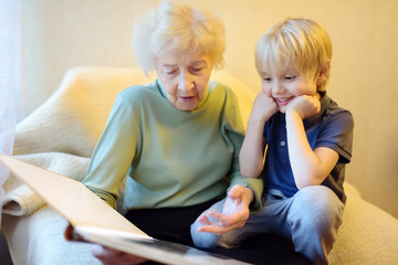 Elderly grandmother and little grandchild looking family photos album. Grandma and grandson. - obrazy, fototapety, plakaty
