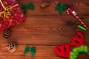 Christmas gift, red present box wrapped with golden ribbon, new year decorations, pine cones, Santa lollipop, deer horns on rustic wooden background. Trendy minimal flatlay, holidays card. Copy space.