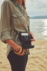 Fashionable woman holding camera on the beach.