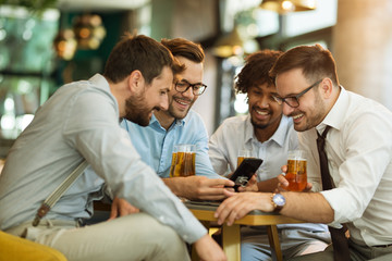 Business people resting in the pub with beer in hands. Having conversation.Funny content on a mobile. Business people resting in the pub with beer in hands. Having conversation.