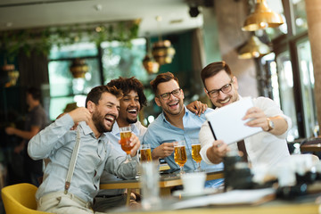 Business people resting in the pub with beer. Having conversation with friends via tablet