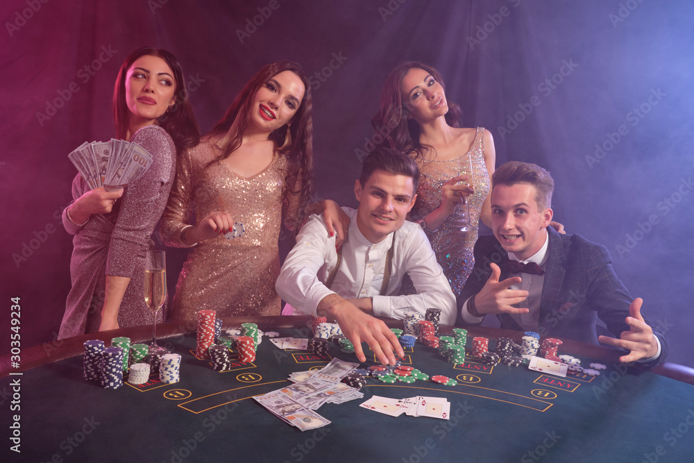 Wall mural friends playing poker at casino, at table with stacks of chips, money, cards on it. celebrating win,