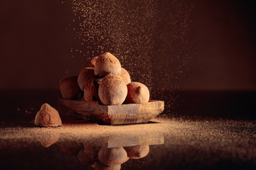 Chocolate truffles in small wooden dish sprinkled with cocoa powder. Black reflective background.