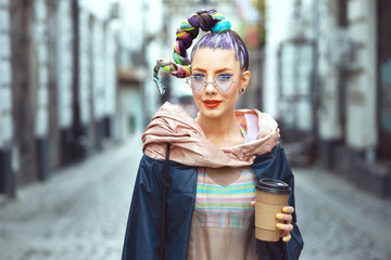 Funky hipster young girl toursit walking city streets holding to go coffee 