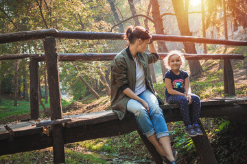 Happy girl with mother relaxing on wooden bridge in the forest.