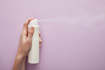 cropped view of woman spraying deodorant on violet background with white roses - obrazy, fototapety, plakaty