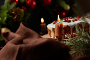 selective focus of traditional Christmas cake with cranberry near burning candles on wooden table