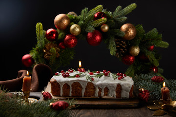 selective focus of traditional Christmas cake with cranberry near Christmas wreath with baubles on wooden table isolated on black