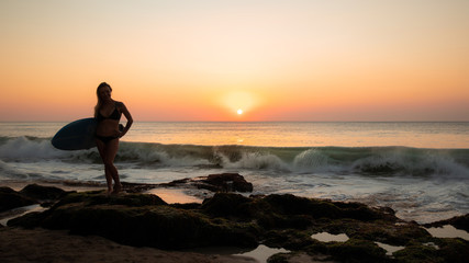 Fototapeta na wymiar Silhouette of surfer girl with surfboard at the beach. Sunset time. Tegal Wangi beach, Bali, Indonesia
