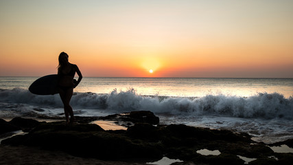 Silhouette of surfer girl with surfboard at the beach. Sunset time. Tegal Wangi beach, Bali, Indonesia