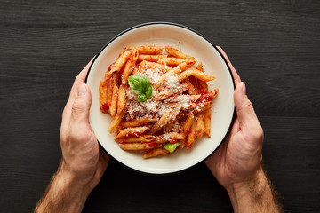 cropped view of man holding plate with tasty bolognese pasta with tomato sauce and Parmesan on...