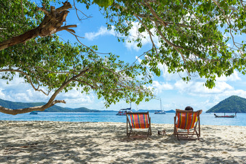 Sunbeds on a paradise island under a tree, sunny day by the sea shore of a resort