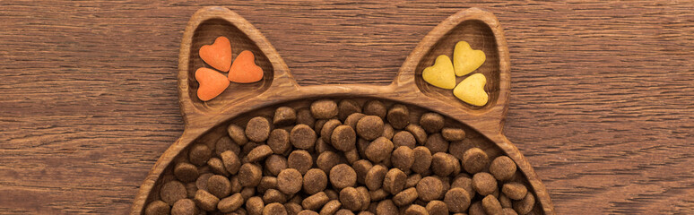 top view of feline dry pet food and vitamins in cat shape plate on wooden table, panoramic shot