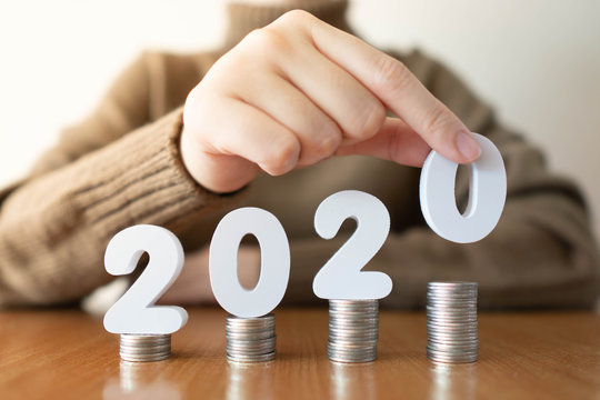 2020 New year saving money and financial planning concept. Female hands putting white number 2020 on stack of coins. Creative idea for business growth, tax payment, investment and banking.
