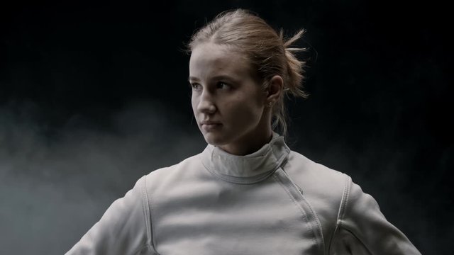 A young pretty woman fencer in the smoky studio