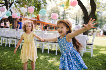 Small girls running outdoors in garden in summer, birthday celebration concept.