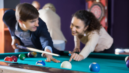 Fototapeta na wymiar young couple hit one ball in billiards, and look at each other. focus on the ball