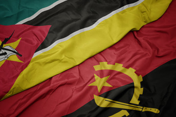 waving colorful flag of angola and national flag of mozambique.
