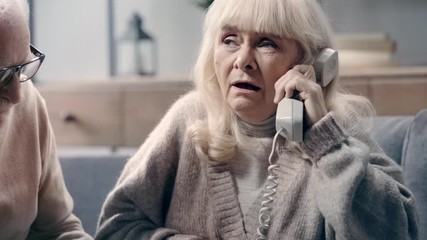 Senior woman with dementia talking on telephone near husband