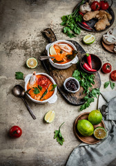 Fototapeta na wymiar Tom Yum soup with shrimps in bowls on shabby beige background with limes, chili pepper, ginger root and mushrooms, ingredients for cooking, copy space