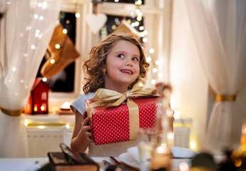 Obraz na płótnie Canvas Cheerful small girl sitting indoors at Christmas, holding present.