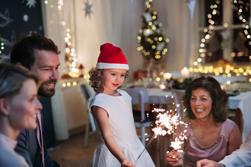 Small girl with parents and grandparents indoors celebrating Christmas.