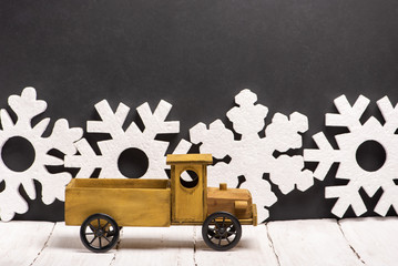 Vintage wooden toy car with an empty body on the background of large white foam New Year’s snowflakes and chalk board