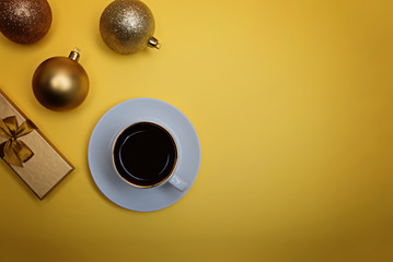 Cup of espresso coffee, golden gift box and golden Christmas balls on a yellow background. Flatlay. View from above.