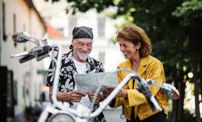 Fototapeta na wymiar A cheerful senior couple travellers with motorbike in town, looking at map.