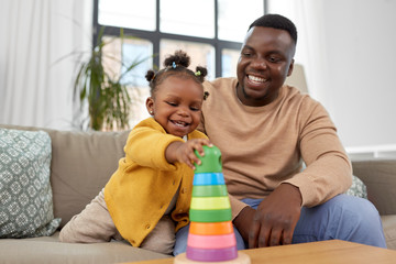 family, parenthood and people concept - happy african american father and baby daughter playing with toy blocks at home