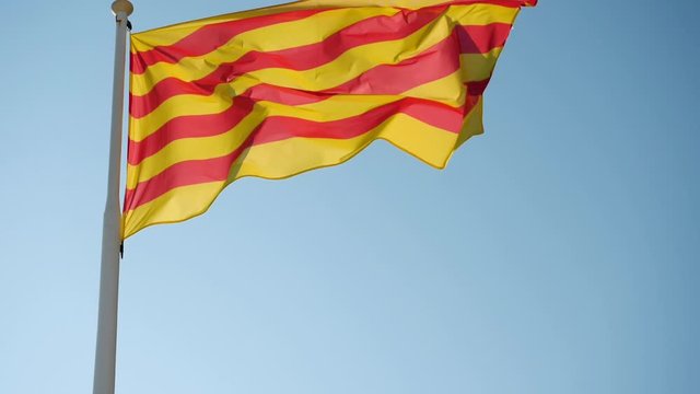 Close-up shot of the flag of Catalonia flying in the wind against blue sky. Barcelona. Spain. Slow motion. HD