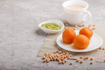 traditional indian candy gulab jamun in white plate with mint chutney on a gray concrete background. side view.