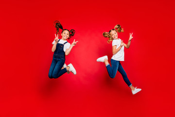 Fototapeta na wymiar Full body photo of two positive blonde brunette hair children girls with tails wait x-mas holidays jump make v-signs wear modern casual t-shirt isolated over red color background