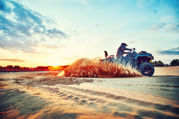 Teen riding ATV in sand dunes making a turn in the sand