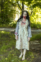 Girl zombie in the blood in the forest on the background of the house