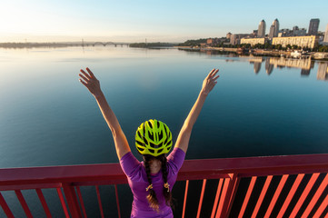 girl cyclist  with a raised hands in the sunset