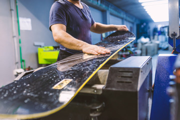 Snowboard tuning and reapair. Winter shop worker doing base repair. Rental workshop service