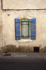 Window of a house with blue painted traditional wooden shutters on a street in Arles, south of France.