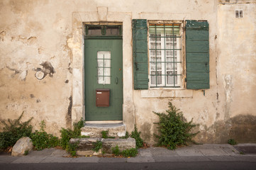 House front with green painted traditional wooden shutters and lace curtains on a street in Arles, south of France.
