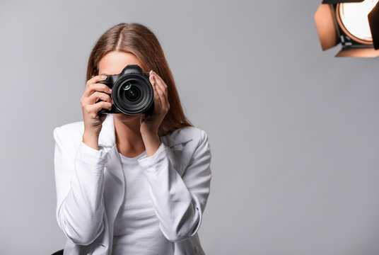 Beautiful female photographer with camera on grey background
