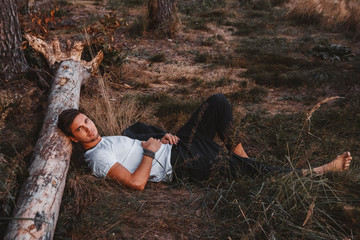 Man lies on the grass, resting his head on a log in the middle of the forest relaxing - resting. Place for text or advertising