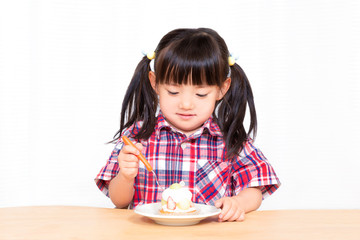 Naklejka premium 白背景でおやつのケーキを楽しそうに食べる幼い女の子。幸せ、成長、健康イメージ