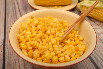 Grains of sweet corn in a plate with a wooden spoon and ears of corn on the table. Healthy diet. Fitness diet. For a sweet treat. Close up.