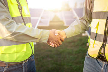 two asian male engineer wearing safety vest handshake with solar panels background. business...