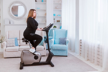 Fototapeta premium Model - a fat woman, at home engaged in a stationary bike.