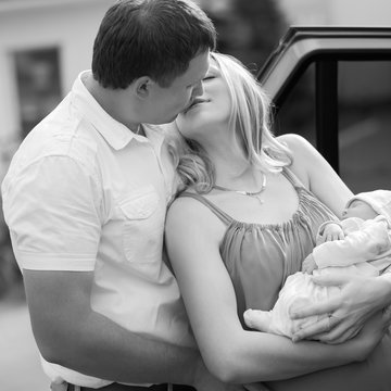 happy husband kissing his wife with a newborn baby