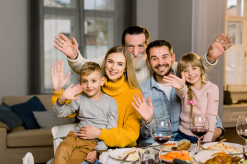 Merry Christmas, Thanksgiving day, Holiday. Happy family are having dinner at home. Grandfather, parents and children sitting together at the table and waving hands, smiling and looking at camera