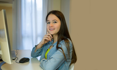 Teen girl working on her homework with the computer, talking on a mobile phone. Side view against a bright glare of the sun from the window.